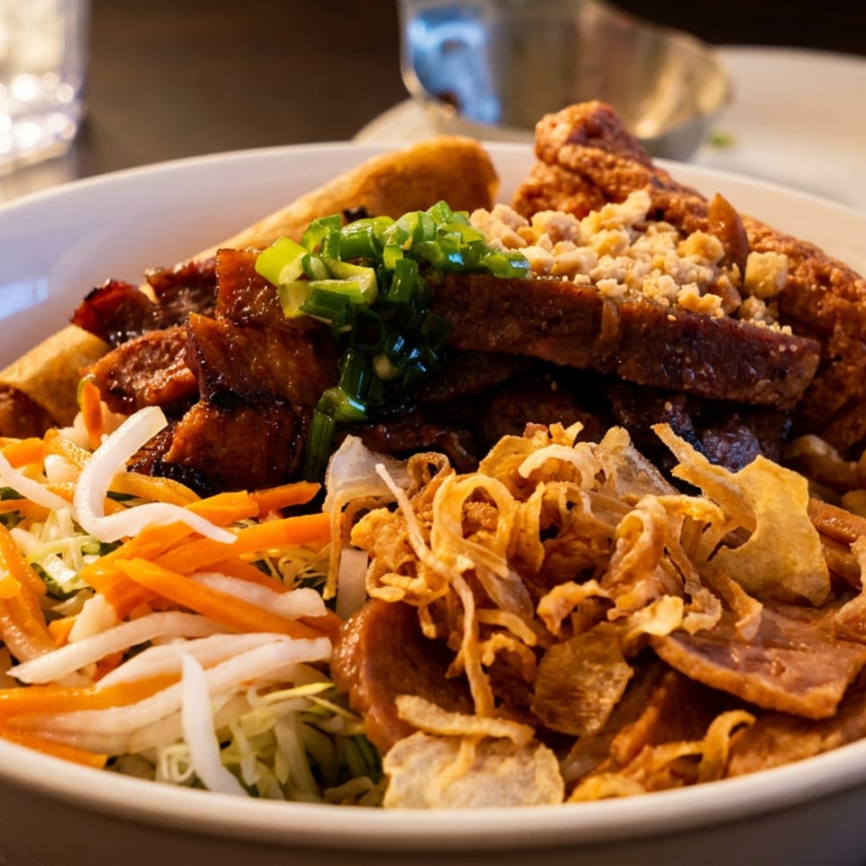 Vietnamese noodle bowl topped with grilled meat, shredded vegetables, crispy fried shallots, peanuts, and green onions.